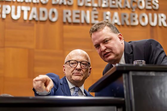 O governador Otaviano Pivetta (Republicanos) sentado e o presidente da ALMT, Max Russi (Podemos), em pé.