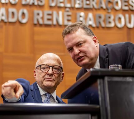 O governador Otaviano Pivetta (Republicanos) sentado e o presidente da ALMT, Max Russi (Podemos), em pé. 